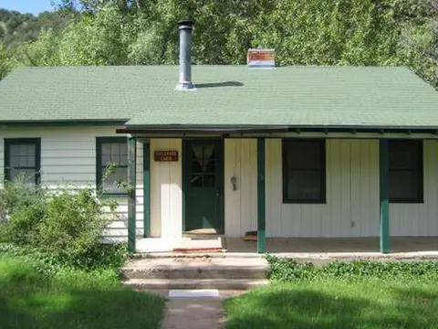 An exterior view of a small cabin with a green roof and porch.