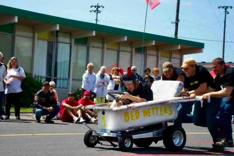 People participate in a bed race event outside a building.