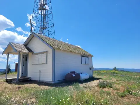 A small white building with a radio tower behind it on a grassy hill.