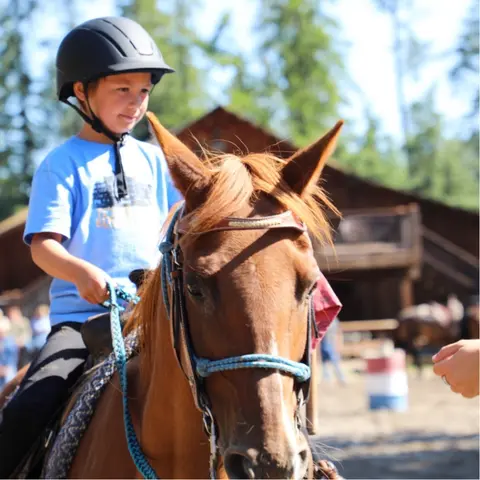 A child wearing a helmet rides a horse outdoors.