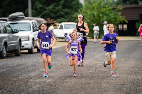 Children and adults run in a race along a dirt road.