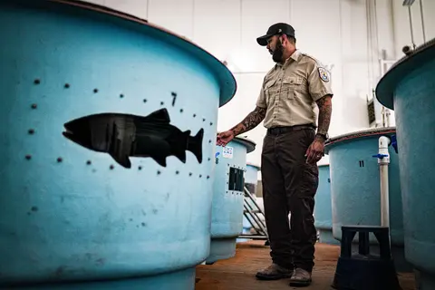 A man in uniform stands next to large blue tanks inside a building.