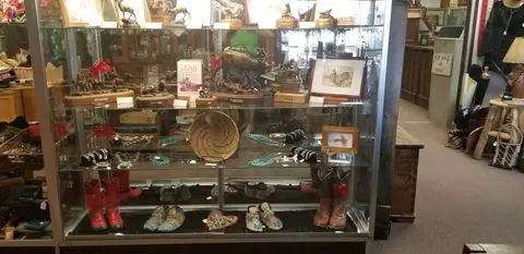 A glass display case in a store holds sculptures, jewelry, pottery, and boots.