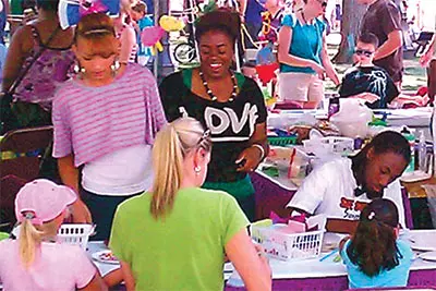 People at tables doing crafts outdoors.