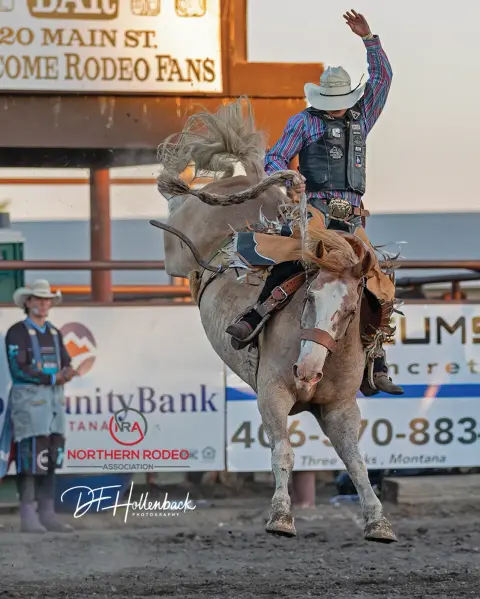 A cowboy rides a bucking horse at a rodeo arena.