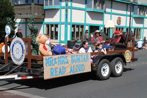 A parade float with people portraying characters and a large sign reading Mr & Mrs Bunyan Read Aloud.