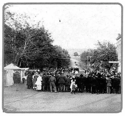 A historic black and white photograph of a crowd gathered outdoors.
