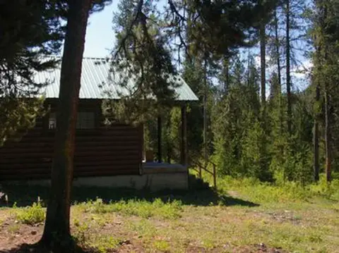 A log cabin stands among trees in a forest.