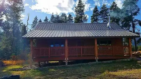 A cabin with a metal roof and a covered porch stands in a forest.