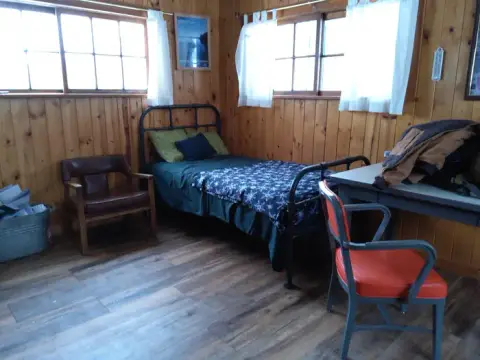 An interior view of a rustic wooden room with a single bed and chairs.