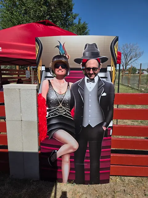 Two people pose in a photo cutout board depicting 1920s attire.