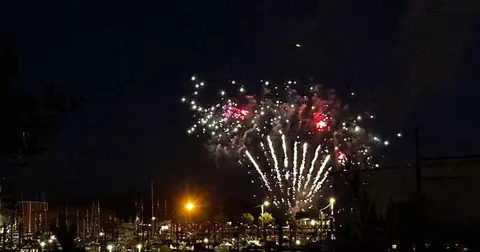 Fireworks illuminate the night sky over a harbor.