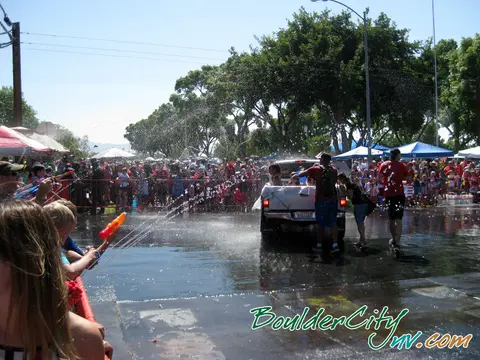 People squirt water at a pickup truck during a crowded outdoor event.