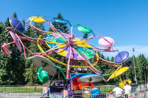 A colorful carnival ride spins against a backdrop of trees and a blue sky.