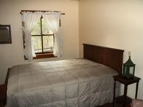 A bedroom with a wooden bed, a nightstand with a lantern, and a window with white curtains.