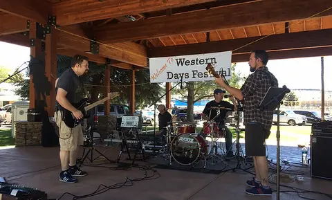 A band performs on a stage under a wooden pavilion.