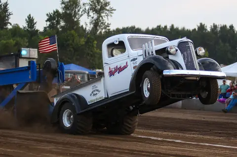 A vintage truck pulls a weighted sled in a tractor pull competition.