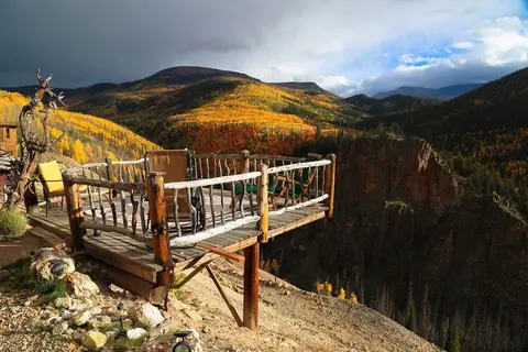 A wooden viewing platform overlooks a scenic mountainous landscape with colorful autumn foliage.