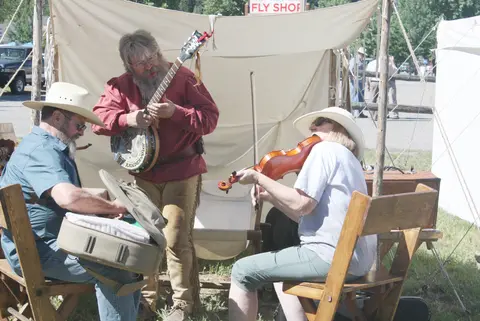 Three people play music outside near tents.