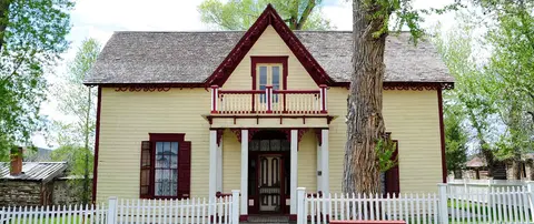 A yellow house with red trim and a white picket fence.