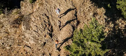 An aerial view of three hikers walking along a rocky mountain trail.