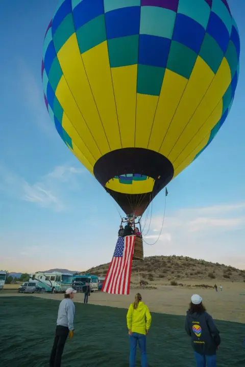 A colorful hot air balloon with an American flag hanging from the basket is preparing for flight.