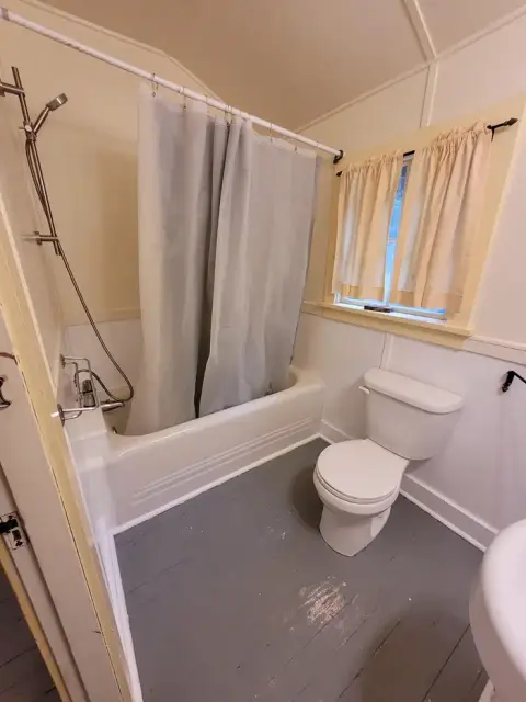 A small bathroom with a bathtub, shower curtain, toilet, and grey painted floor.