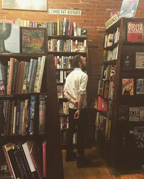 A man browses books between tall wooden shelves in a bookstore.