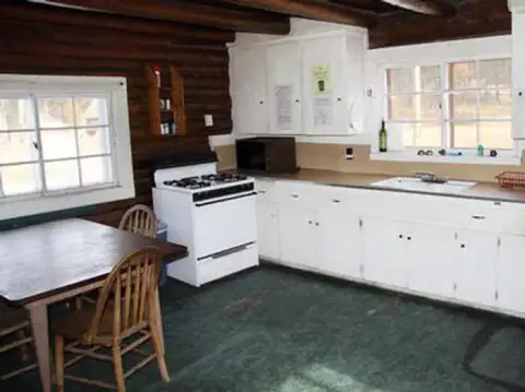 Interior of a rustic kitchen with log walls and white cabinets.