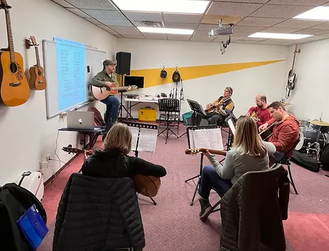 A group of people sitting in a circle playing guitars in an indoor studio space.