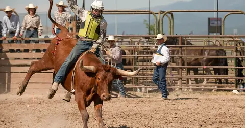 A cowboy rides a bucking bull in an arena during a rodeo.