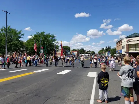 A color photograph of a parade on a sunny day with people watching from the street.