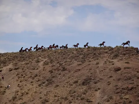 Metal horse sculptures stand along a ridge against a cloudy sky.