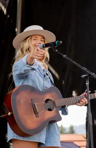 A woman singing and playing acoustic guitar on stage.