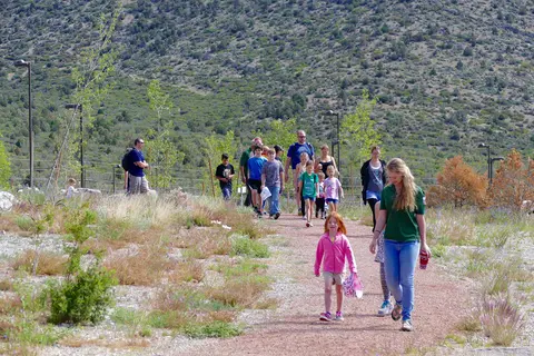 A group of people walks along an outdoor trail in a natural landscape.