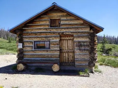 A rustic log cabin sits outdoors in a clearing.