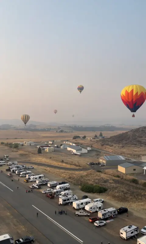 An aerial view of several hot air balloons flying over a landscape with parked RVs.