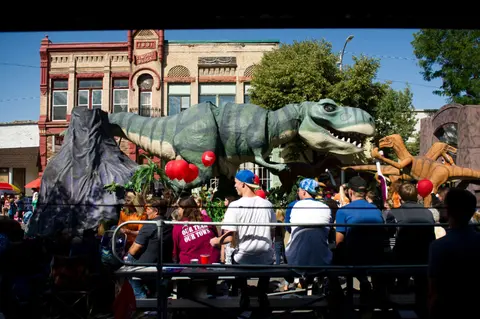 A crowd watches a parade float featuring large dinosaur models.