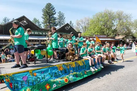 A school band rides and plays instruments on a decorated float in a parade.