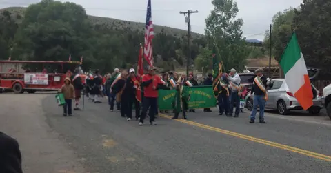 People walking in a parade down a street carrying flags and banners.