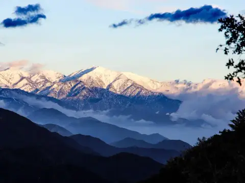 A scenic view of snow-capped mountains with clouds and layered foothills.