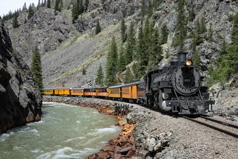 A steam train travels along a rocky river canyon.