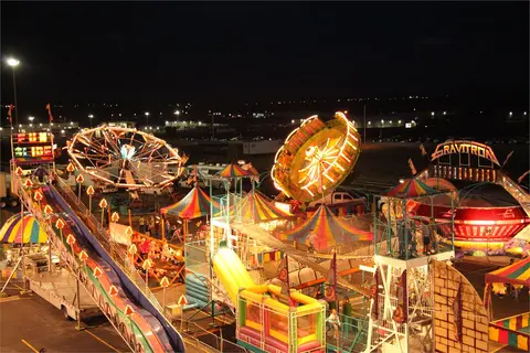 An illuminated carnival at night featuring various rides and attractions.