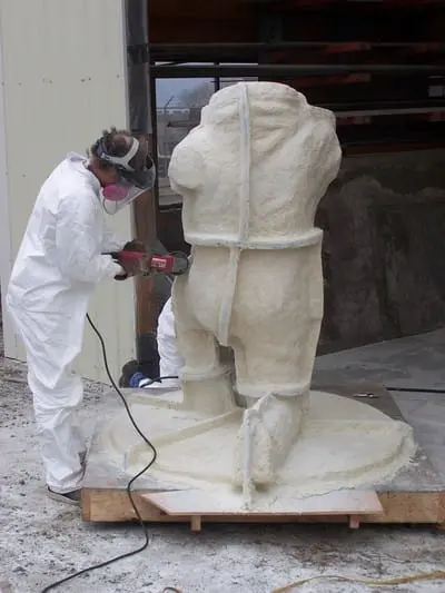 A person in a protective suit and mask works on a large sculpture.