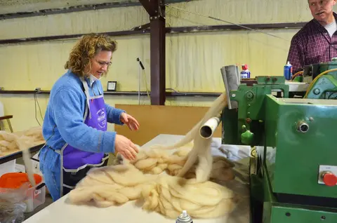 A woman works with wool coming out of a machine indoors.