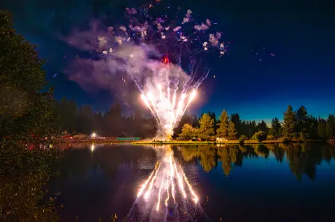 Fireworks explode over a lake at night.