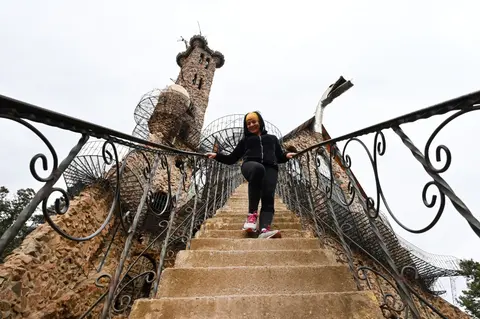 A person descends stone stairs with ornate iron railings in front of a unique stone tower structure.