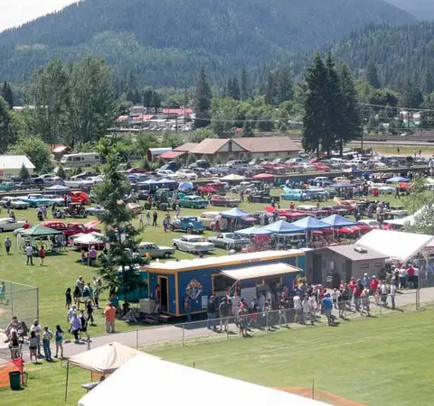An outdoor gathering with numerous classic cars parked on a grassy field and people walking around.