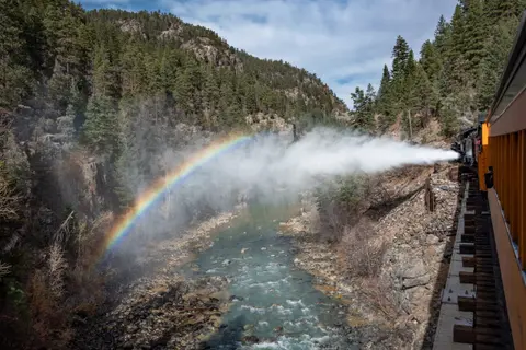 A train travels along a canyon railway while spraying water that forms a rainbow.