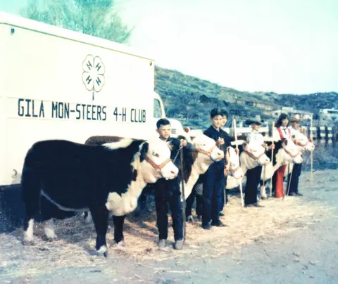 A vintage photo of children standing with their cattle next to a club truck.